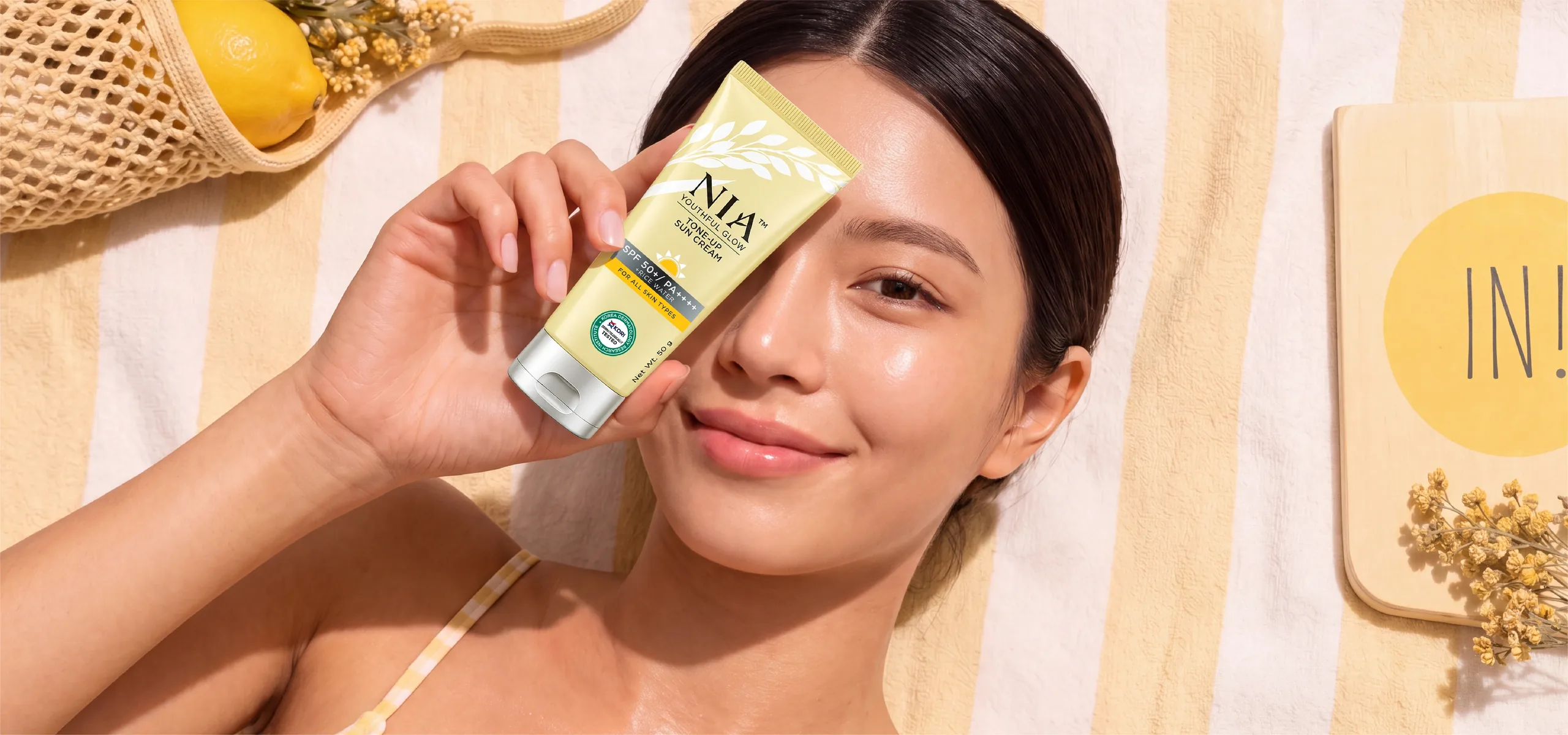 NIA Tone-Up Sun Cream SPF 50+ poolside flatlay with model